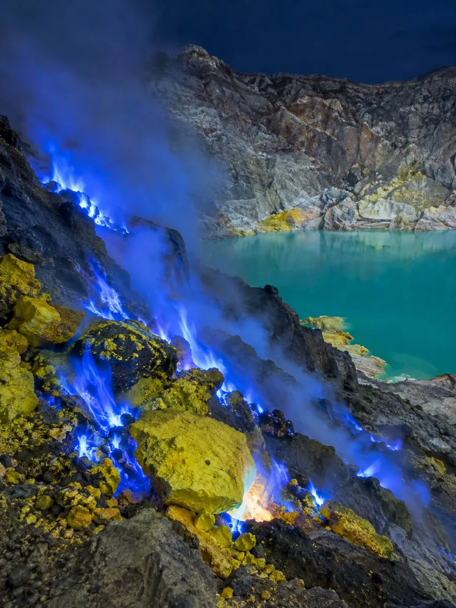 Des flammes bleues brûlant au-dessus des roches de soufre jaune la nuit à l'intérieur du cratère de l'Ijen